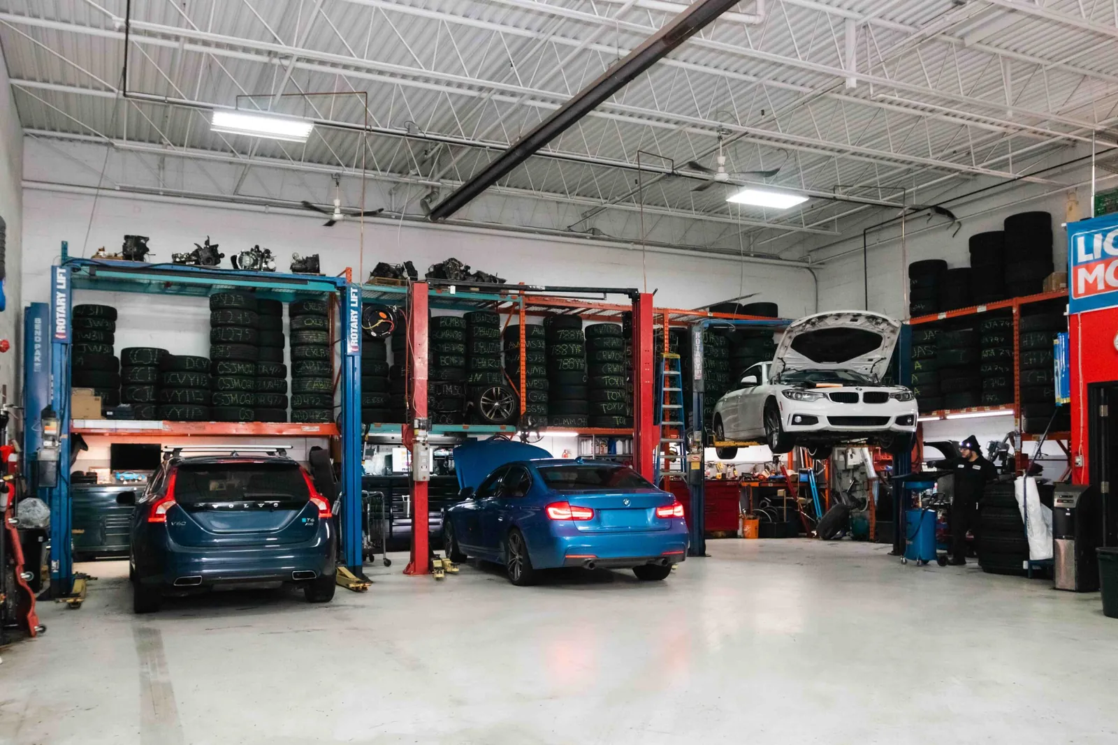 The White Eagle Motors service floor in Mississauga: a Volvo wagon and a blue BMW sedan in the bays, a white BMW up on a lift, and tires racked along the walls